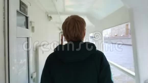 金发人沿着船甲板沿着栏杆走船在晴朗的晴天航行莫斯科河后视图男的头视频的预览图