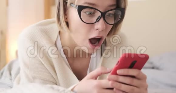 令人惊讶的女人在床上用手机视频的预览图