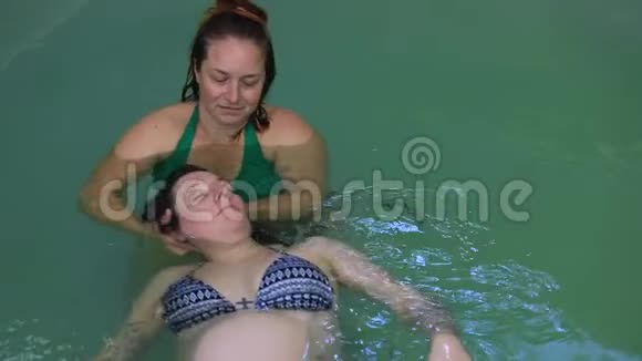 孕妇和教练一起在游泳池里漂浮视频的预览图
