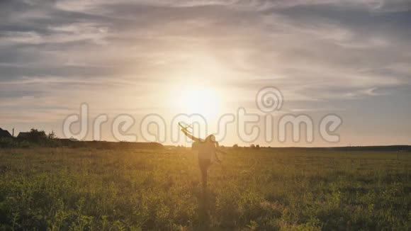 一个年轻的女孩带着一架玩具飞机在夕阳的天空下奔跑视频的预览图