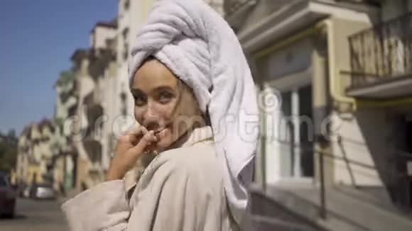 幸福自信的年轻女子穿着浴袍头上戴着毛巾走在街上喝着咖啡转过身来视频的预览图