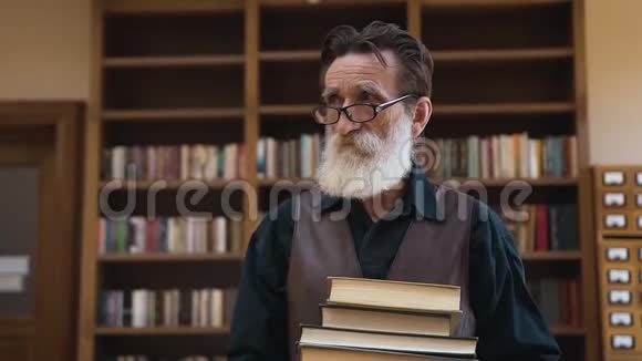 聪明的大胡子老人手里拿着许多书从图书馆里走了进来视频的预览图