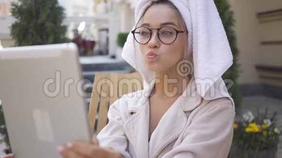戴眼镜穿浴袍头戴毛巾坐在后院看平板电脑的美女画像视频的预览图