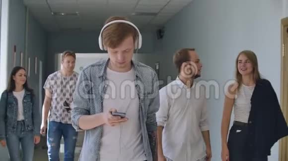 一个男人听着音乐走在学院的大厅里看着智能手机的屏幕视频的预览图