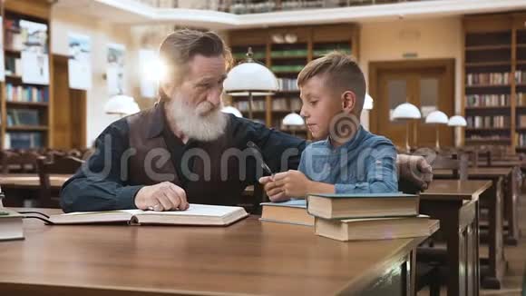 英俊聪明的胡子爷爷和他的小孙子一起在图书馆里度过时光视频的预览图