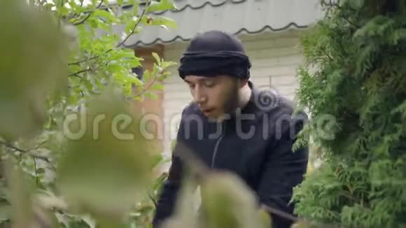 一个穿着黑色衣服的年轻白人小偷闯入家门前藏在树下的画像那家伙要视频的预览图