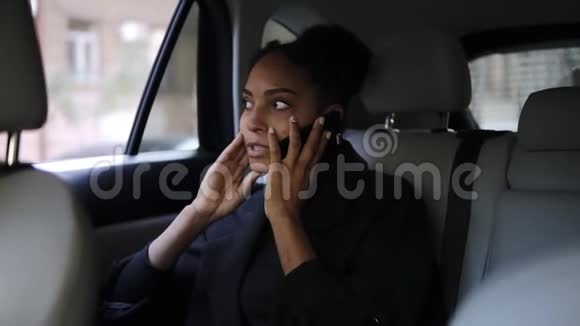 一位漂亮的美国黑人女商人坐在出租车后座上坐在一个带着明亮皮革沙龙的出租车上在她的移动电话旁交谈视频的预览图