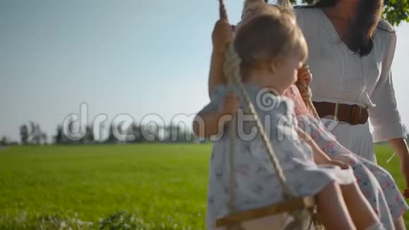 妈妈摇着两个小妹妹一岁和三岁用绳子把手在木秋千上视频的预览图