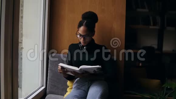 这位年轻有魅力的美国黑人妇女正在大窗台上看书时尚的特写肖像视频的预览图