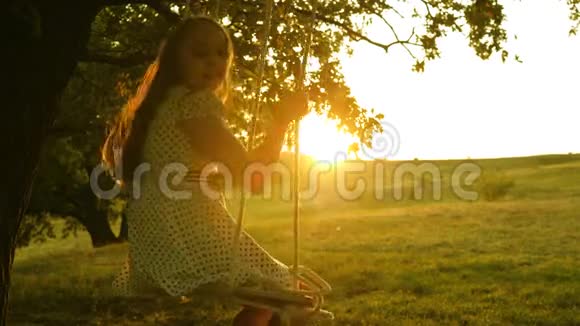 快乐的童年概念孩子在日落公园的橡树枝上飞绳秋千女孩笑高兴年轻女孩视频的预览图
