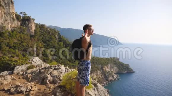 男子徒步旅行者背着背包站在边缘山欣赏美丽的海景享受旅行的人快乐视频的预览图