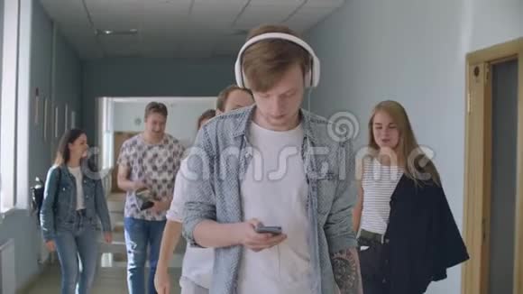 一名男子戴着耳机在一群学生中听音乐在大学走廊上视频的预览图