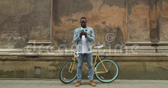 美国黑人男子在现代自行车前使用智能手机和微笑的耳机中的全身射击视频的预览图