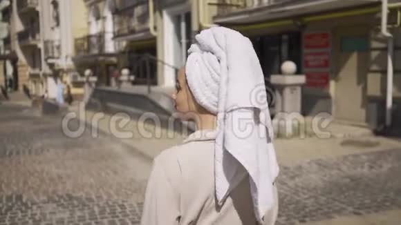 年轻女子穿着浴袍头上戴着毛巾走在街上喝着咖啡自信的女孩喜欢视频的预览图