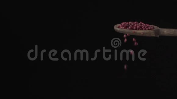 红色胡椒在黑色背景下缓慢地从木勺倒入底部视频的预览图