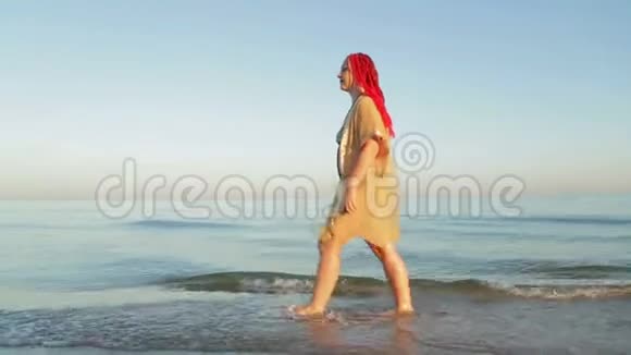 一个穿着泳衣和黄色浴袍的女人在海边散步视频的预览图