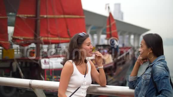 年轻女子在码头边谈笑风生船后扬起红帆视频的预览图