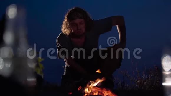 晚上坐在河岸上的年轻人吹篝火希普斯特在大自然中放松视频的预览图