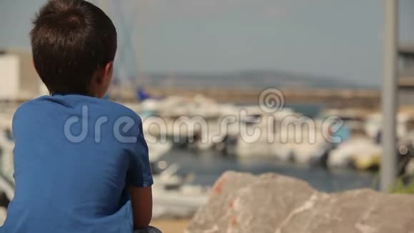 男孩坐在石头上用游艇看着海湾视频的预览图