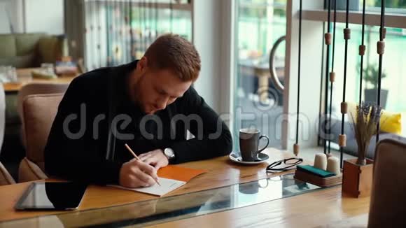 年轻的帅哥在笔记本上写字在舒适的咖啡馆里写字视频的预览图