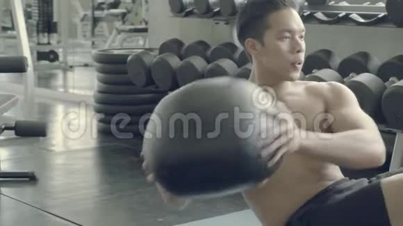 年轻的亚洲男人在健身房里用举重锻炼身体用健身球锻炼男性视频的预览图