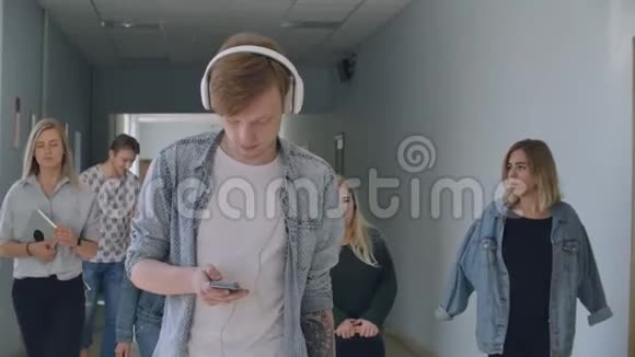 一个戴耳机的年轻人沿着倒置走廊走听音乐不注意人它视频的预览图