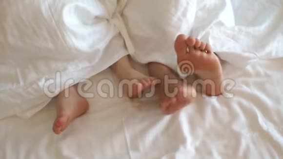 妈妈的脚和一个小孩床上一条白色毯子下面的特写视频的预览图