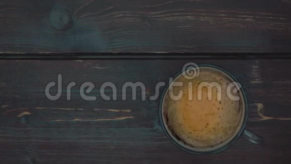 咖啡泡沫在玻璃杯中与咖啡一起旋转桌子的深褐色表面上往下看视频的预览图