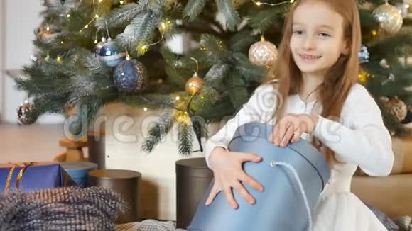可爱的金发女孩打开了深蓝色的礼物盒她坐在圣诞树旁快乐的童年和圣诞节视频的预览图