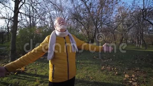 在公园里的一个温暖的秋日里一个双手向上旋转的老人在散步时享受空气和阳光视频的预览图