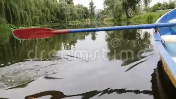 在湖上的马鞍和小船碎片有百合花和莎草绿色城市公园湖上划着小木蓝的小船b部分视频的预览图