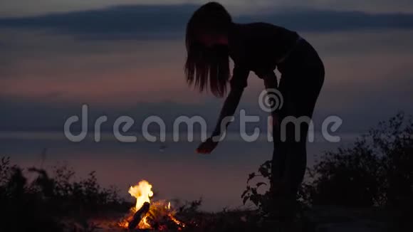 年轻迷人的女孩在海边与篝火做棉花糖与火在舒适的夏季晚上视频的预览图