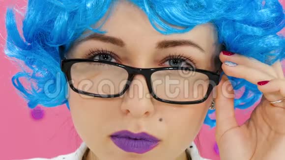 戴着蓝色假发和戴着深红色背景眼镜的女孩的肖像视频的预览图