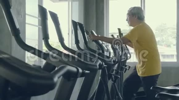 老年人在健身房锻炼亚洲年长的白种人在椭圆机健身运动中做有氧运动视频的预览图