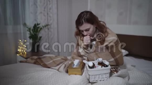 病毒的症状生病的年轻女人用滴在鼻子上坐在沙发上用温暖的格子毯子颤抖视频的预览图