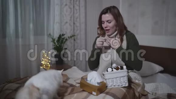 生病的年轻妇女在床上拿着餐巾纸和药品打喷嚏和咳嗽因为对猫过敏或流感视频的预览图