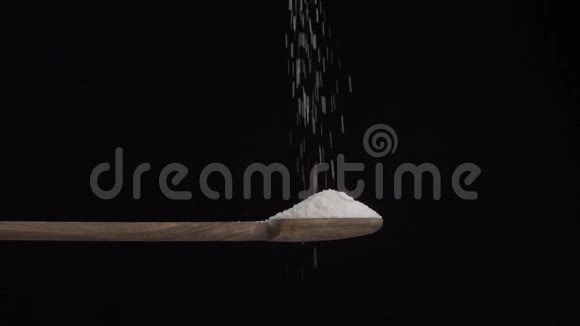 盐从上面倒入一个木勺放在黑色的背景上视频的预览图