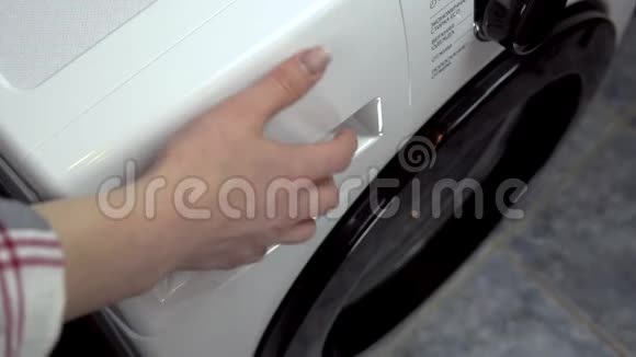 一个年轻的女人把洗涤剂倒进洗衣机里一个女人把粉末和液体倒入一个特殊的隔间视频的预览图