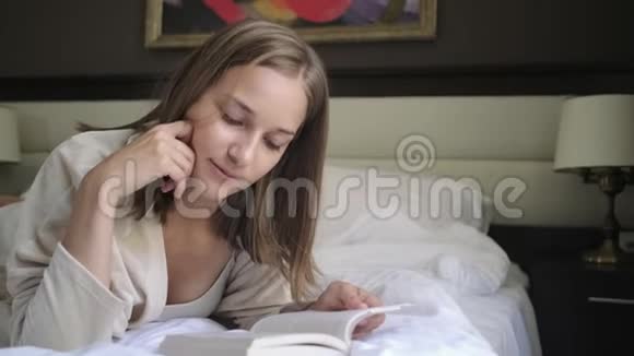 年轻女子在床上靠着墙上的画读书视频的预览图