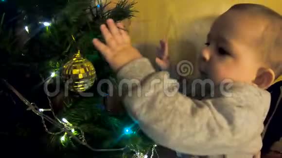 一个小到一岁的孩子婴儿玩新年树触摸花环和玩具他对什么很感兴趣视频的预览图