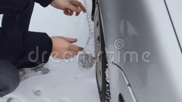 冬天白天男人从他的车上取下一个塑料轮毂盖天气又坏又冷特写镜头故障或视频的预览图
