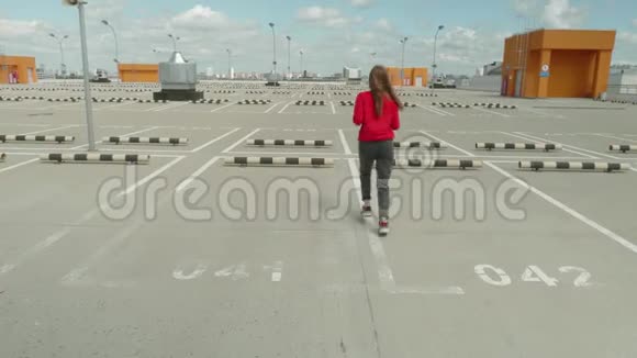 穿着红色连帽衫和黑色牛仔裤的女孩在贸易中心屋顶的空停车场上奔跑视频的预览图