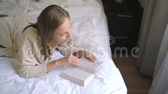 年轻的金发女人躺在大床上看书视频的预览图