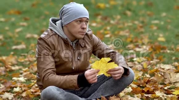 那家伙坐在公园里的落叶上小心翼翼地拿起一片黄色的枫叶仔细地检查着它视频的预览图