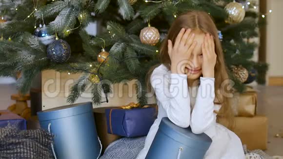可爱的金发女孩收到了一个深蓝色的礼物盒坐在圣诞树附近快乐的童年和圣诞节庆祝视频的预览图