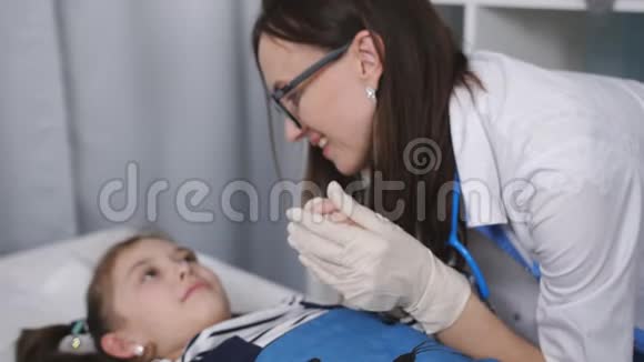 微笑友好的女医生与躺在医院病床上的儿科医生办公室里的小病人交谈视频的预览图