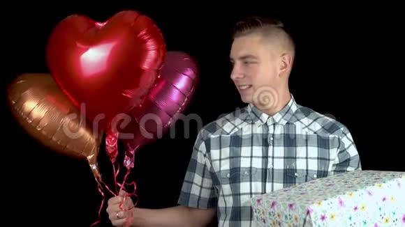 一个年轻人拿着礼物和心形气球站着一个人手里拿着一份礼物和装有氦气的球视频的预览图