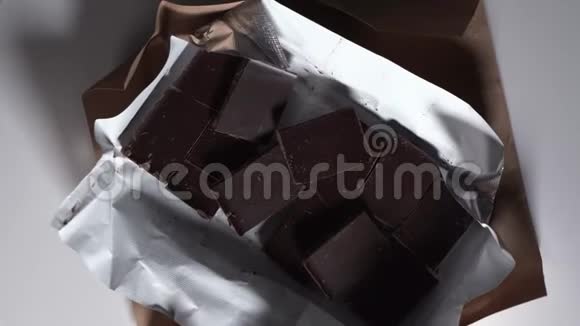 在包装中打开的巧克力棒上俯视黑巧克力旋转旋转在白色的桌子上甜点在桌子上视频的预览图
