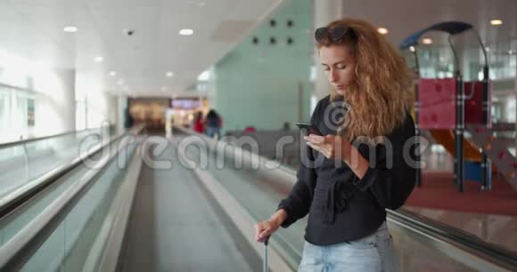 坐自动扶梯的女人在国际机场拿着行李用手机视频的预览图