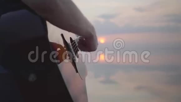 在夏日海滩附近的傍晚五彩缤纷的日落背景下嬉皮士年轻人弹吉他唱歌关门视频的预览图